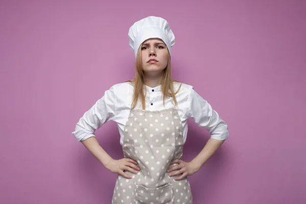 漂亮而严肃的女孩 穿着制服 粉色背景 穿着厨房衣服的家庭主妇画像 复制空间 — 图库照片