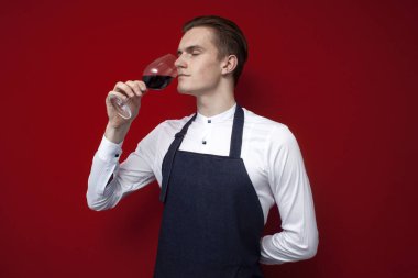 Genç şarap garsonu renkli bir arka planda kırmızı şarap içer. Bir uzman şarabın tadını alır ve elinde bir bardak tutar.