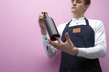 Üniformalı genç profesyonel garson pembe arka planda bir şişe kırmızı şarap tutuyor ve yakın plan mesaj için bir yer arıyor.