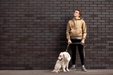 Genç adam elinde av köpeğiyle duvarın arkasında duruyor ve mesaj atmak için bir yere bakıyor.