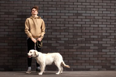 Köpekli genç adam sokakta duvarın arkasında duruyor ve gülümsüyor, boşluğu kopyalıyor.