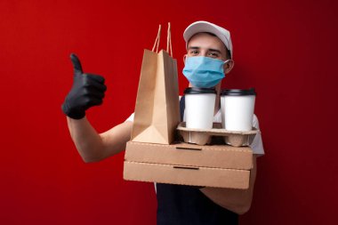 Koruyucu maskeli ve eldivenli genç yemek teslimatçısı kutuları tutuyor ve Coronavirus salgını sırasında doğum yaptığını gösteriyor.