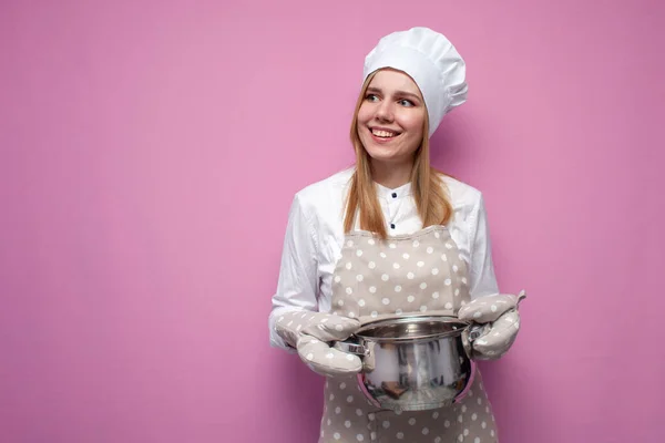 young cheerful girl cook in kitchen clothes holds a pan, smiles and looks at a place for text, happy woman housewife cooked lunch, copy space