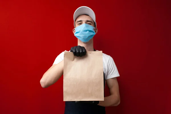 Koruyucu maskeli ve eldivenli genç adam boş bir çanta hazırlıyor. Coronavirus sırasında bir paket tutuyor.