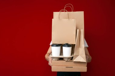 Yemek dağıtım elemanı kırmızı arka planda bir sürü paket, kutu ve paket tutuyor. Fast food paketleme, fotokopi alanı.