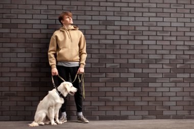 Genç adam elinde av köpeğiyle duvarın arkasında duruyor ve mesaj atmak için bir yere bakıyor.