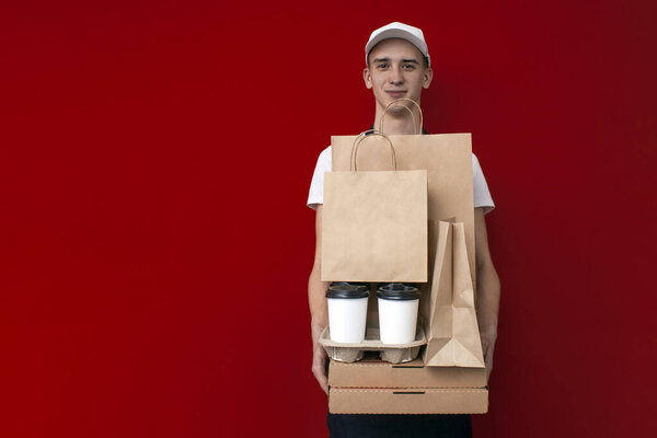 food delivery man holds a lot of packages, boxes and parcels on a red background, packaging from fast food, copy space