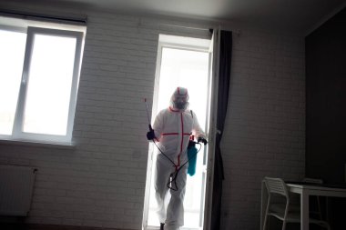 Dairede koronavirüs dezenfeksiyonu. Koruyucu giysili insanlar odayı virüslerden ve hastalıklardan, enfeksiyon temizleme servisinden profesyonel olarak temizliyorlar.
