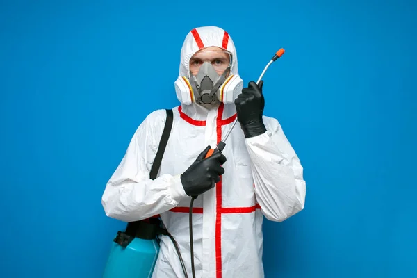 防護服を着たプロの消毒剤男は青い隔離された背景にスプレーボトルを保持しています設備のある消毒サービスワーカー コロナウイルスの概念 — ストック写真