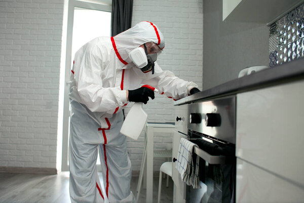 человек в защитном костюме и респираторе вытирает мебель химическим агентом, дезинфицирует помещение, санитарно-гигиенические работы
