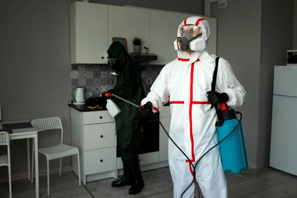 防護服とマスクを着た人々がアパートを化学薬品で消毒し衛生労働者がコロナウイルスから部屋をきれいにし消毒サービス — ストック写真