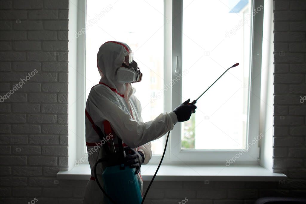 disinfection at home. A man in a protective suit cleans the window with a chemical agent, protecting the house from coronavirus