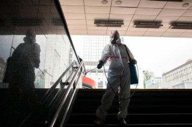 Koronavirüs salgını. Koruyucu giysili dezenfekte işçisi ve solunum cihazı sokakta kimyasal spreyle tırabzanlara tutunuyor.