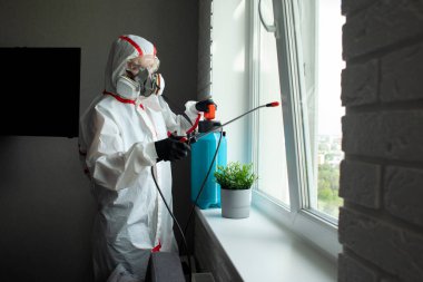 Odanın kimyasal temizliği, koruyucu giysili ve solunum cihazlı bir kişi dairedeki enfeksiyonları kimyasal bir maddeyle temizliyor.