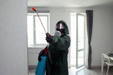 Odanın kimyasal temizliği, koruyucu giysili ve solunum cihazlı bir kişi dairedeki enfeksiyonları kimyasal bir maddeyle temizliyor.