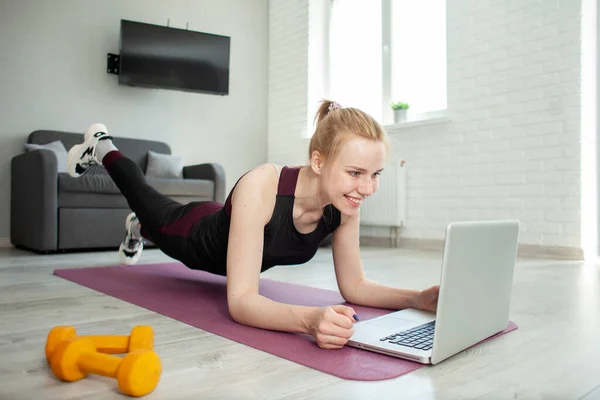 Genç sporcu kız spor için eve gidiyor ve dizüstü bilgisayarla video eğitimi izliyor, sporcu sabahları spor yapıyor ve online eğitim, kendini izole etme konseptini izliyor.