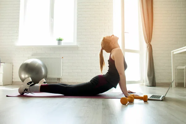 Sport at home. a young girl watches an online tutorial on a laptop and does an exercise on flexibility in a room, an athlete doing yoga on self-isolation