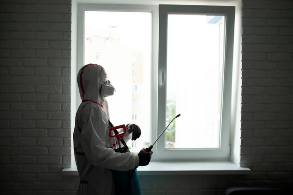 家庭での消毒 防護服を着た男が化学物質で窓をきれいにし 家をコロナウイルスから保護します — ストック写真