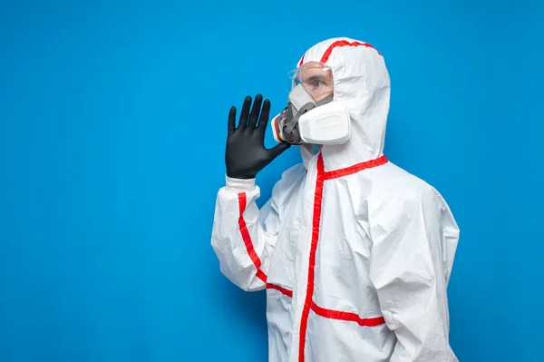 disinfection worker in protective suit and respirator screaming in panic, virologist on blue isolated background, coronavirus pandemic