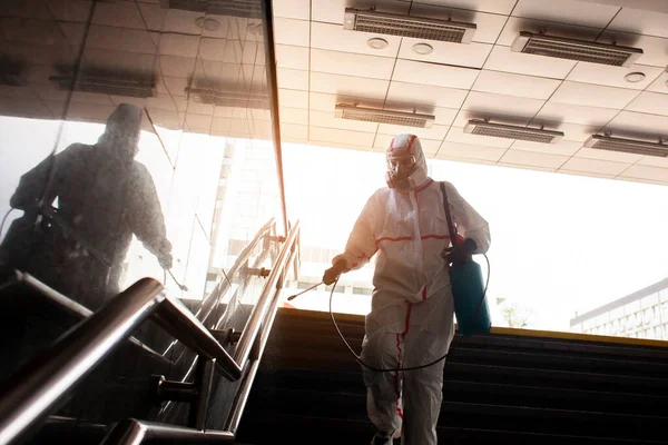 disinfection of the city from coronavirus, a man in a protective suit and respirator cleans the handrails of the stairs with a chemical spray, a sanitary worker, chemical treatment