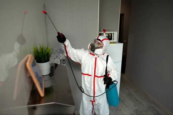 Koruyucu giysili ve solunum cihazlı bir adam daireyi kimyasal bir maddeyle dezenfekte ediyor. Temizlik işçisi de Coronavirus 'tan odayı temizliyor.