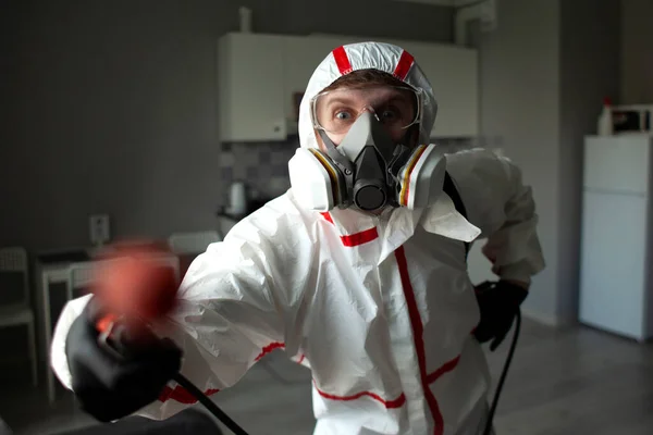 man in a protective suit and respirator disinfects the apartment with a chemical agent, a sanitation worker cleans the room from coronavirus, close-up