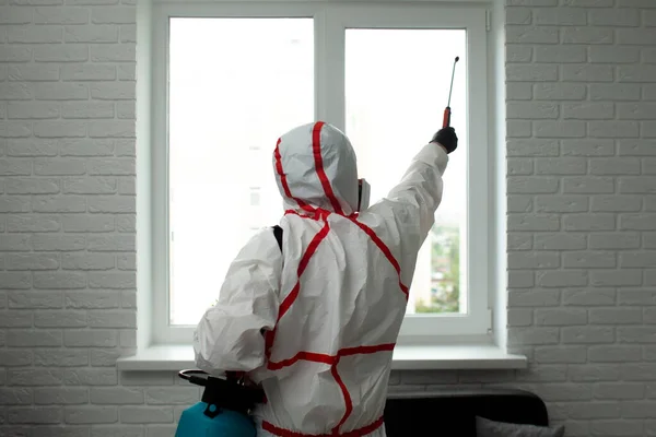 在家里消毒 一名身着防护服的男子用化学剂擦拭窗户 以保护房子不受考拉韦的侵袭 — 图库照片
