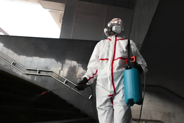 coronavirus pandemic, a man in a protective suit and a respirator cleans the street with a chemical agent, sanitary work in the city, chemical treatment