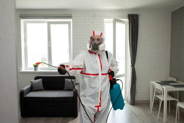 コロナウイルスからの部屋の消毒 防護服を着た男が化学物質で感染症のアパートを清掃する衛生清掃サービス — ストック写真