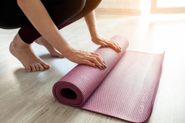 Yoga zamanı. Yalınayak kız evde yoga minderini açıyor, sporcu kadın yoga yapmaya hazır, yakın plan.