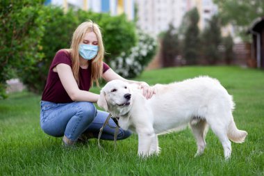 Coronavirüs salgınında köpeği gezdiren genç bir kız. Parkta köpek yavrusuyla maske takan bir kadın.