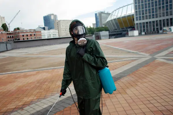 disinfection of the city from coronavirus, a man in a protective suit and a respirator on the street against the background of the city, a sanitary worker, chemical treatment