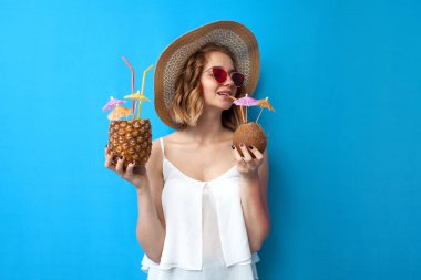 Yaz kıyafetleri içinde genç bir kız ananas ve hindistan cevizinden yapılmış tropikal kokteyller içiyor.