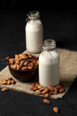 Siyah bir zemin üzerinde cam şişelerde badem sütü, fındıklı, şekersiz vejetaryen sütü, dikey çerçeve