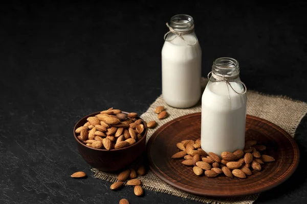 almond milk in glass bottles on a dark black background with nuts, vegetarian milk without sugar and lactose