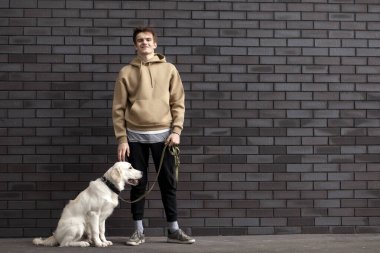 Köpekli genç adam sokakta duvarın arkasında duruyor ve gülümsüyor, boşluğu kopyalıyor.