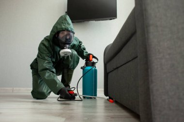 Haşere kontrolü. Koruyucu giysili bir işçi, hamamböcekleri ve farelerden sprey tabancayla odayı temizliyor, temizlik servisi de daireyi kimyasal bir maddeyle dezenfekte ediyor.
