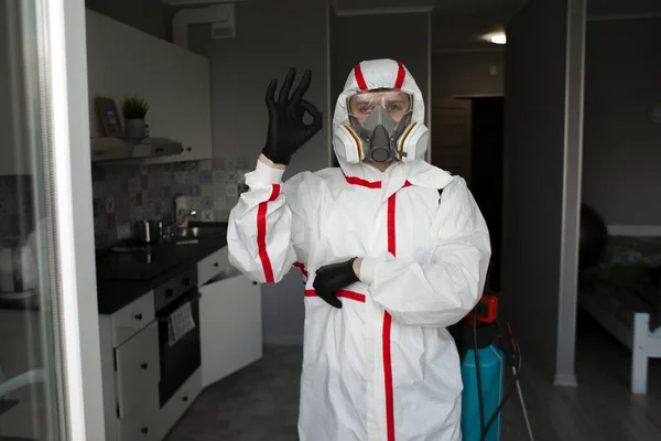 pest control. Worker in a protective suit stands in the background of the apartment and shows okay, disinfection of the room, clean apartment