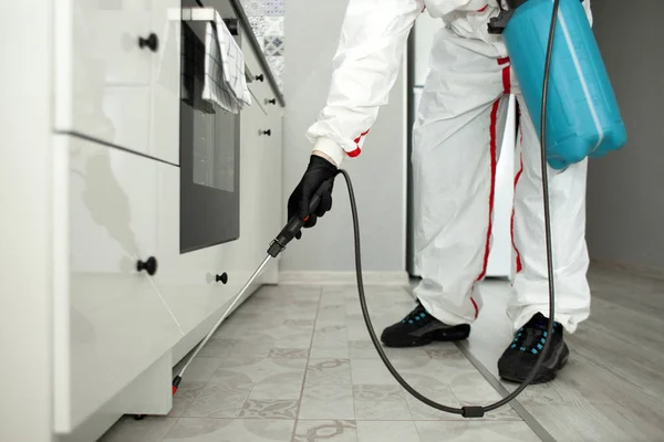 pest control. A worker in a protective suit cleans the shelves in the kitchen from cockroaches and ants with a spray, the sanitary service disinfects the room with a chemical agent