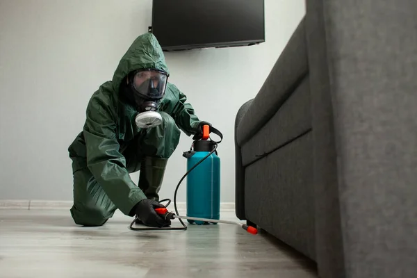 pest control. A worker in a protective suit cleans the room from cockroaches and rats with a spray gun, the sanitary service disinfects the apartment with a chemical agent