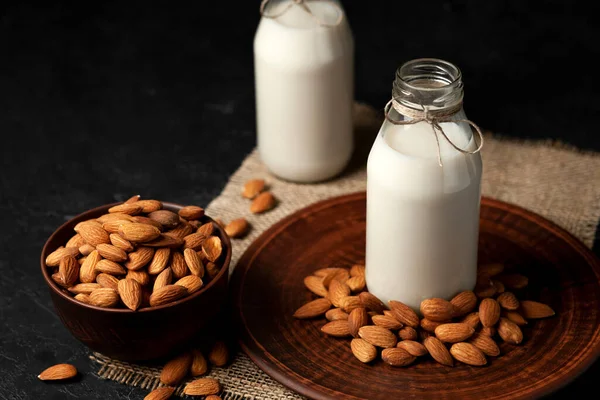 almond milk in glass bottles on a dark black background with nuts, vegetarian milk without sugar and lactose, close-up