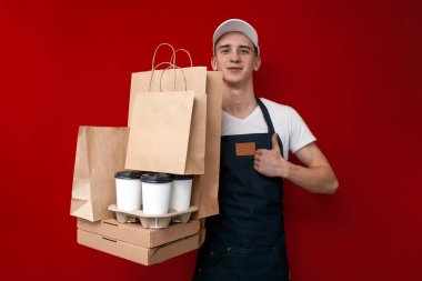 Genç adam üniformalı bir teslimatçı bir sürü ambalaj ve kutu fast food taşıyor ve siparişi büyüleyici bir çalışanın teslim ettiğini gösteriyor.