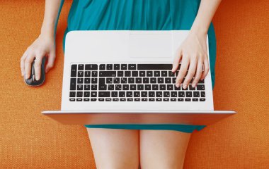 Kanepede dizüstü bilgisayarla oturan genç bir kadının en iyi görüntüsü.