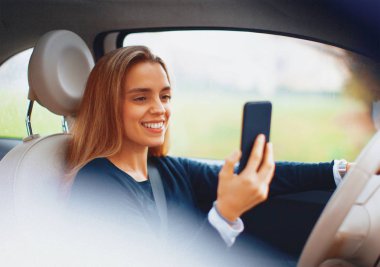 Yeni arabasında gülümseyen genç sarışın kadın. Arabadaki akıllı telefonu kullan.