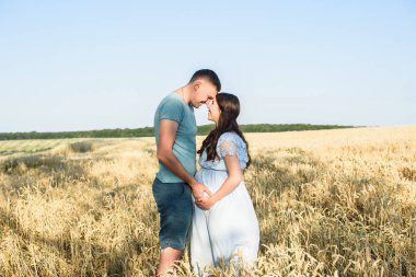 Bir buğday alanında romantik hamile çift portre. Hamile kadın kocasıyla doğada rahatlatıcı güzel güneşli bir günde ayakta