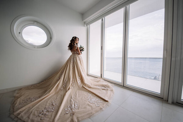 невеста с длинным поездом в белой комнате с панорамным видом на море
.