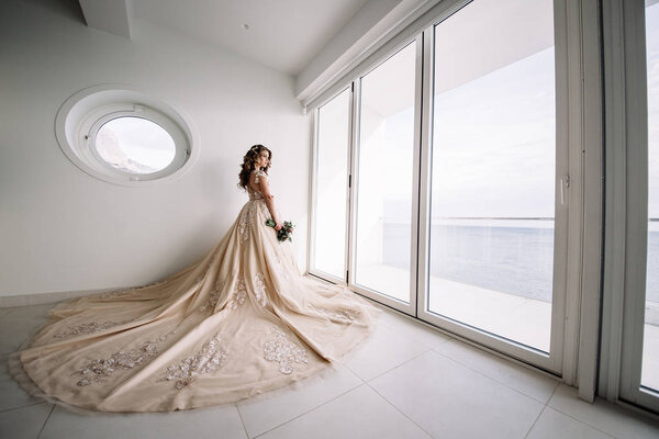 невеста с длинным поездом в белой комнате с панорамным видом на море
.