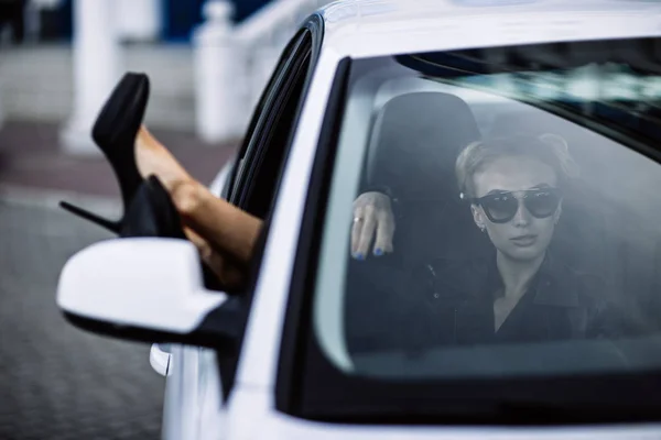 Foto al aire libre de moda de mujer hermosa sexy con pelo oscuro en chaqueta de cuero negro y gafas de sol posando en auto de lujo — Foto de Stock