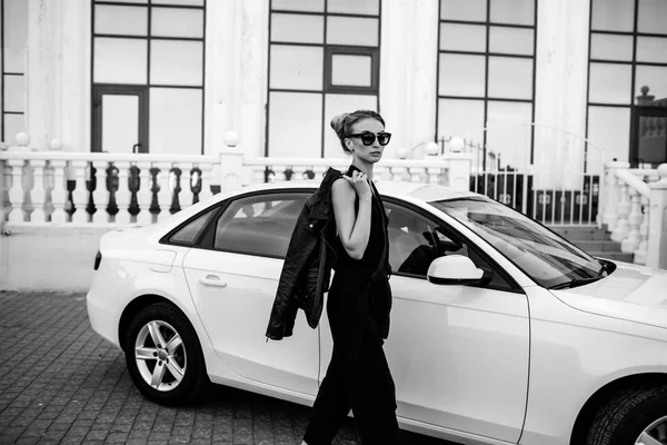 Foto al aire libre de moda de mujer hermosa sexy con pelo oscuro en chaqueta de cuero negro y gafas de sol posando en auto de lujo — Foto de Stock