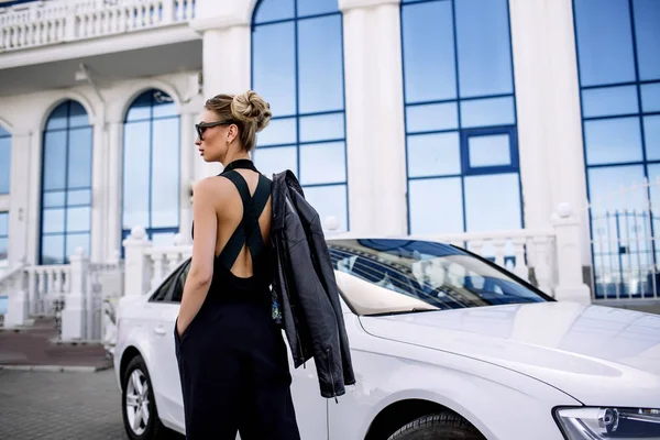 Photo de mode en plein air de belle femme sexy aux cheveux foncés en veste en cuir noir et lunettes de soleil posant en voiture de luxe — Photo
